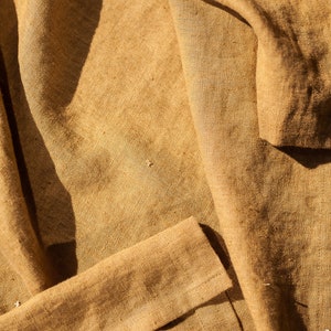 May include: A close-up of a brown fabric with a textured surface. The fabric is folded and has a natural, rustic look.