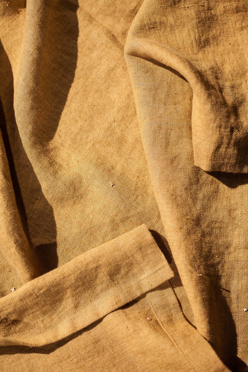 May include: A close-up of a brown fabric with a textured surface. The fabric is folded and has a natural, rustic look.