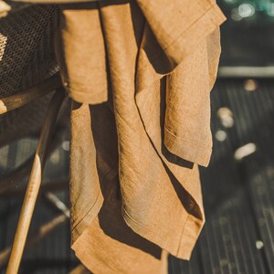 May include: A brown linen throw draped over a wicker chair with a brown straw hat on top.