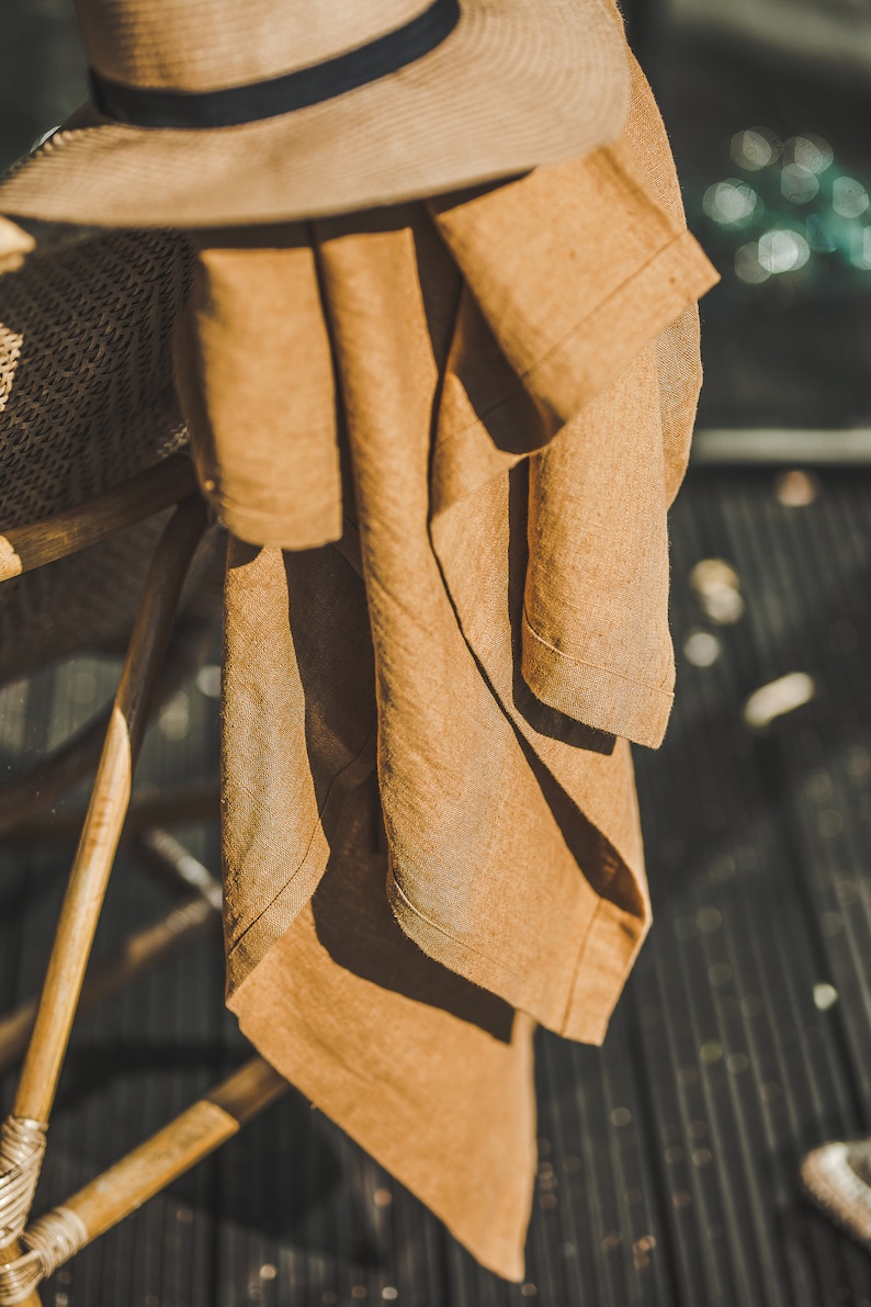 May include: A brown linen throw draped over a wicker chair with a brown straw hat on top.