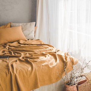 Pu&ograve; includere: Un copriletto in lino giallo senape con una gonna da letto in lino bianco. Il letto &egrave; fatto con due cuscini, uno bianco e uno giallo senape. Il letto &egrave; davanti a una finestra con tende bianche trasparenti.
