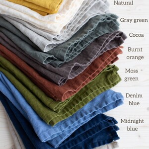 May include: A stack of 12 linen napkins in various colors, including mimosa yellow, cream, natural, gray green, cocoa, burnt orange, moss green, denim blue, midnight blue, and sand.