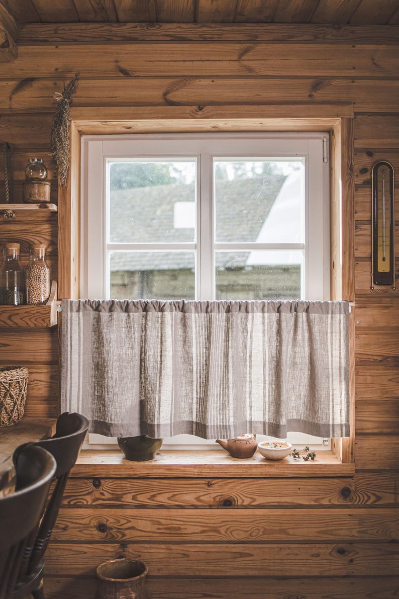 May include: A window with a white frame and a linen curtain with gray stripes. The window is in a room with wood paneling. There is a teapot and a bowl on the windowsill.