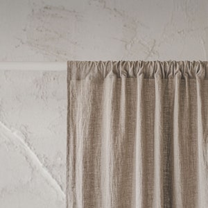 May include: A beige curtain with a visible woven texture hanging from a white rod. The fabric features vertical pleats created by the rod pocket header, resulting in consistent folds that extend downward from the top support structure.