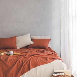 Pu&ograve; includere: Un copriletto in lino color ruggine con una gonna da letto in lino bianco e due cuscini bianchi e ruggine. Una tazza e un croissant sono su un vassoio sul letto. Un cesto di vimini pieno di libri &egrave; sul pavimento accanto al letto.