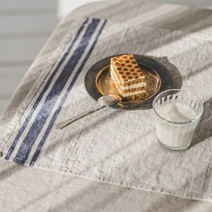 May include: A close-up of a piece of layered cake on a silver plate with a spoon, a glass of milk, and a blue and white striped linen napkin on a beige tablecloth.