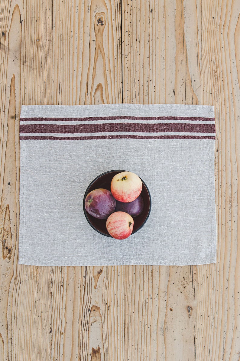 May include: A bowl of red and purple apples on a striped linen placemat. The bowl is black and the apples are arranged in a cluster.