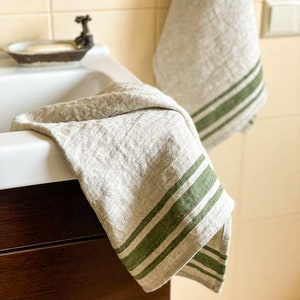 Puede incluir: Dos toallas de cocina de lino con rayas verdes colgadas de un gancho y drapeado sobre un lavabo de ba&ntilde;o.