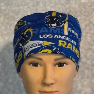 May include: Blue and yellow surgical scrub hat with a repeated pattern of the Los Angeles Rams logo, the team name, and "Los Angeles Rams".