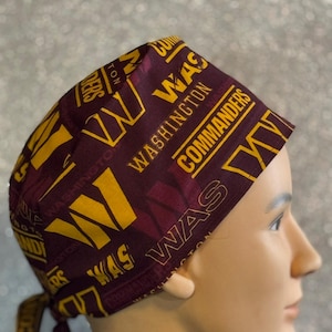 May include: A burgundy and gold surgical scrub hat with the Washington Commanders logo and team name repeated throughout the fabric.