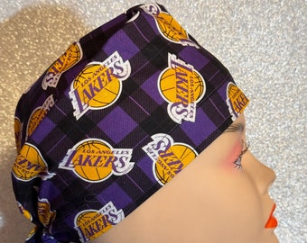 May include: Purple and black patterned surgical scrub hat with the Los Angeles Lakers logo repeated throughout. The hat has a tie at the back.