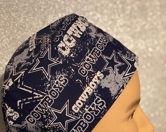 Puede incluir: Una cubierta para la cabeza con estampado azul marino y blanco con la palabra "COWBOYS" y gráficos de estrellas. La cubierta para la cabeza está diseñada para atarse en la parte posterior.