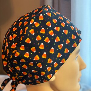May include: Black scrub hat with a candy corn pattern. The hat has a tie at the back.