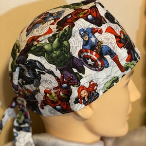 May include: A white scrub hat with a tie, featuring a colorful print of various Marvel superheroes, including Iron Man, Hulk, Captain America, and Black Widow.