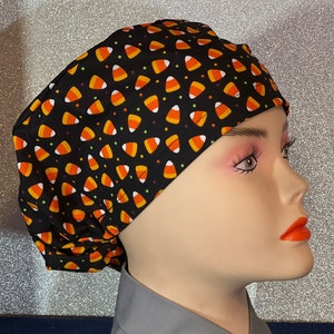 May include: Black scrub hat with a pattern of orange and white candy corn on a black background.