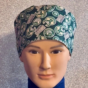 May include: A green and white patterned cap featuring the Milwaukee Bucks logo and text. The cap is worn by a mannequin. The cap has a dark green background with white and green logos and text.