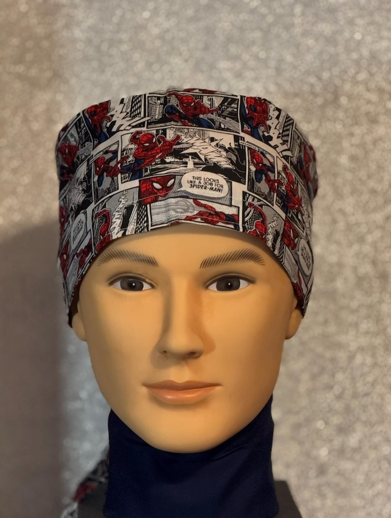 May include: A white and black scrub hat with a comic book print featuring Spiderman. The text on the hat reads "This looks like a job for Spider-Man!"