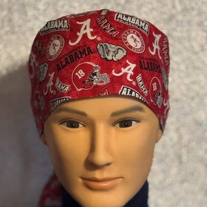 May include: Red and white patterned surgical scrub hat with the University of Alabama logo and the words "Alabama" and "Crimson Tide".