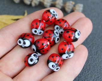 Può includere: Una collezione di perline di vetro rosse e nere a forma di coccinella con occhi bianchi. Le perline hanno un diametro di circa 1 cm.
