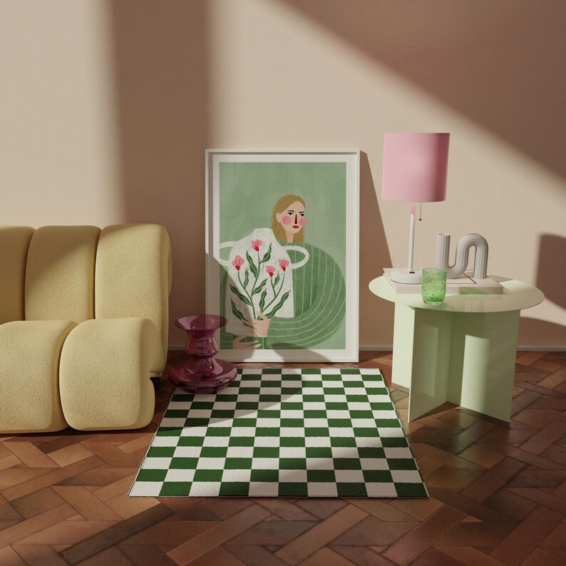 May include: A green and white checkered rug with a framed illustration of a woman holding a vase of pink flowers. The illustration is set against a green background. A pink lamp with a white base sits on a light green side table.