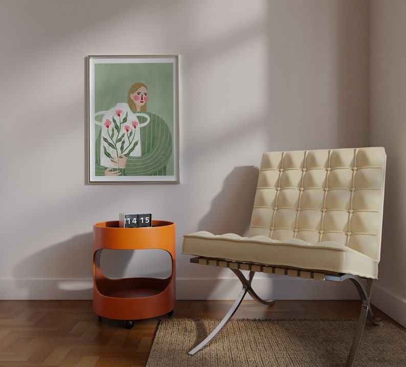 May include: A framed illustration of a person holding a bouquet of pink flowers. The illustration is set against a green background. A clock displaying 14:15 is on a small orange side table. A white chair with a tufted back is in the foreground.