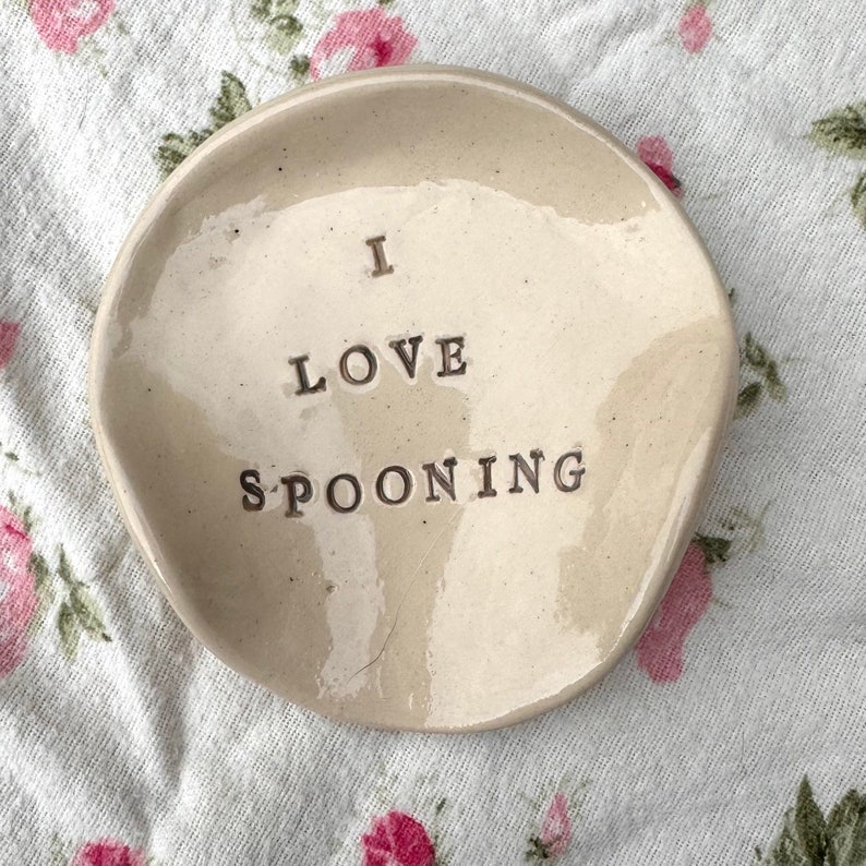 Op de afbeelding: Een witte keramische lepelsteun met de tekst "I love spooning" in bruine letters.