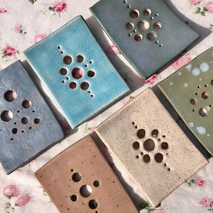 May include: Six ceramic soap dishes with a geometric pattern of circles. The dishes are in various colours, including blue, green, brown, and white.