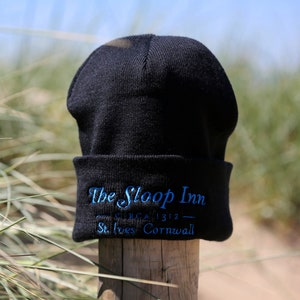 May include: Black knitted beanie with a blue embroidered logo that reads "The Sloop Inn - Circa 1312 - St. Ives Cornwall".