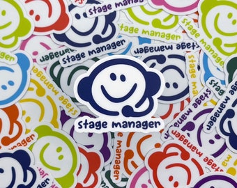 May include: A collection of colorful stickers with a smiling face wearing a headset. The stickers are in various colors, including blue, green, red, and purple. Each sticker has the words "stage manager" printed on it.