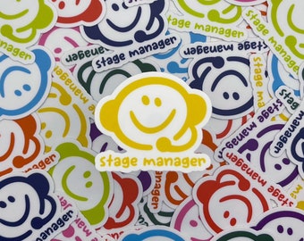 May include: A collection of colorful stickers featuring a smiling face with a headset and the words "stage manager." The stickers are in various colors, including yellow, blue, green, and red, with a white background.