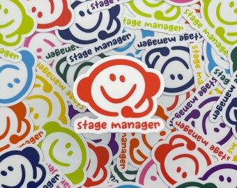 May include: A collection of colorful stickers featuring a smiling face with a headset and the words "stage manager." The stickers are in various colors, including red, blue, green, and purple, with white outlines.