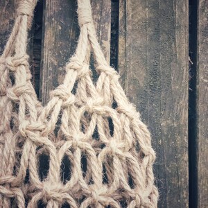 May include: A close-up of a beige rope macrame hanging bag against a weathered wooden background.