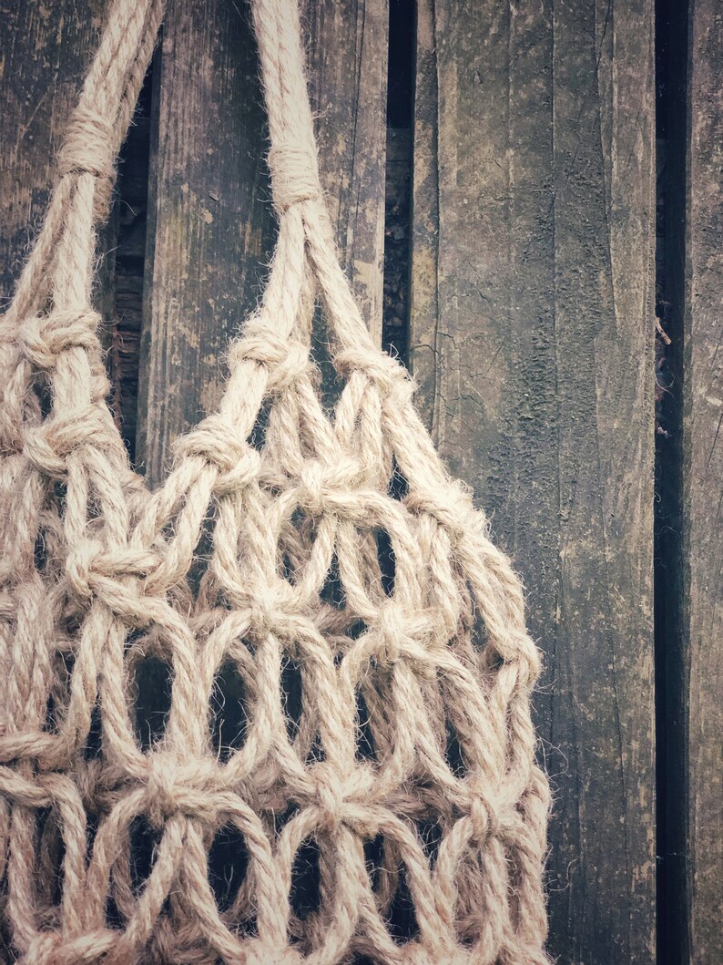 May include: A close-up of a beige rope macrame hanging bag against a weathered wooden background.
