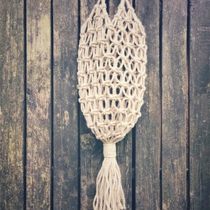 May include: A beige crocheted string bag with a long tassel hanging from a wooden surface.