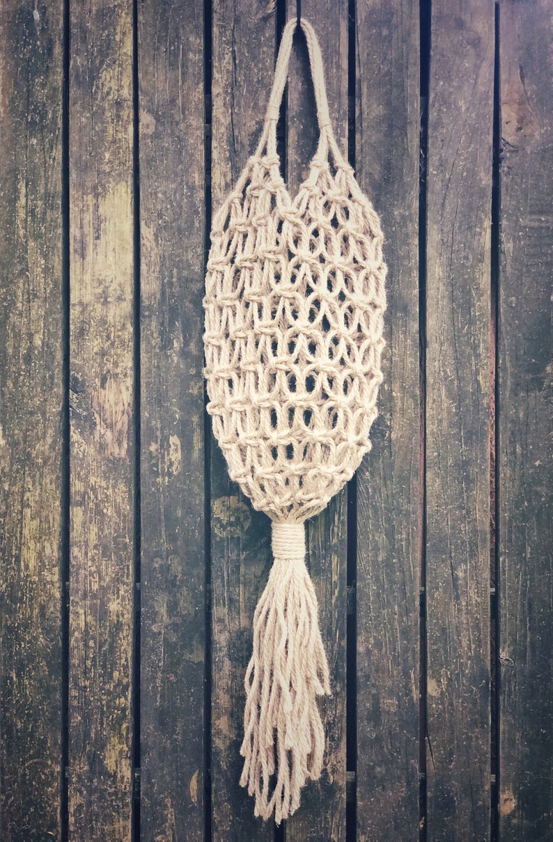 May include: A beige crocheted string bag with a long tassel hanging from a wooden surface.