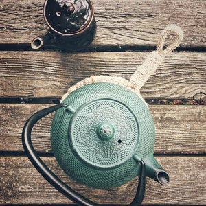 May include: A green cast iron teapot with a black handle and a brown teapot with a lid on a wooden surface.