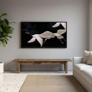 May include: A living room scene featuring a large black framed TV displaying a white and gray crane illustration against a black background. A wooden bench sits below the TV, with a white sofa and a potted plant to the left.