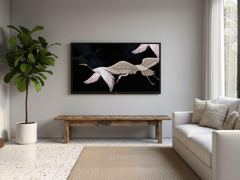 May include: A living room scene featuring a large black framed TV displaying a white and gray crane illustration against a black background. A wooden bench sits below the TV, with a white sofa and a potted plant to the left.