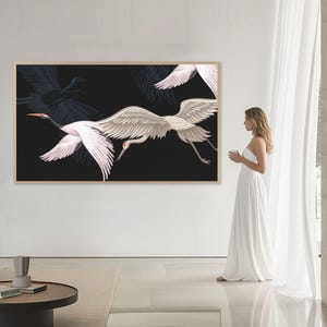 May include: A large framed artwork featuring white and gray cranes in flight against a black background. The artwork is displayed on a white wall in a modern living space. The cranes have outstretched wings, and the artwork is in a light-colored wooden frame.