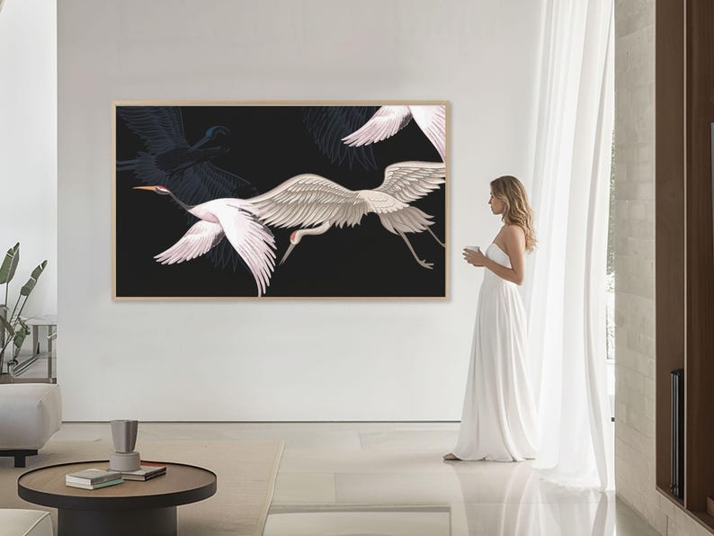 May include: A large framed artwork featuring white and gray cranes in flight against a black background. The artwork is displayed on a white wall in a modern living space. The cranes have outstretched wings, and the artwork is in a light-colored wooden frame.