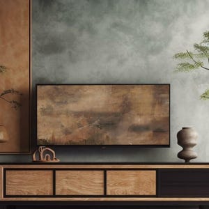 Könnte beinhalten: Ein modernes Wohnzimmer mit einem hölzernen Entertainment-Center, auf dem ein Flachbildfernseher mit einem gedämpften braunen abstrakten Bild auf dem Bildschirm steht. Der Fernseher ist an der Wand über dem Entertainment-Center montiert. Eine kleine Holzskulptur steht auf dem Entertainment-Center links vom Fernseher. Eine dunkelgraue Keramikvase steht auf dem Entertainment-Center rechts vom Fernseher. Die Wand hinter dem Fernseher ist hellgrau mit einer strukturierten Oberfläche.