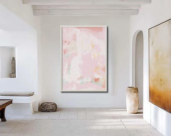Op de afbeelding: Een abstract schilderij in een witte lijst domineert een lichte, minimalistische kamer. Het kunstwerk toont zachte roze, witte en lichtgroene penseelstreken. De kamer omvat een stenen sculptuur, een houten tafel en een groot, neutraal getint tapijt.