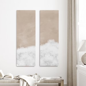 Può includere: Due tele verticali. La parte superiore di ogni tela è beige chiaro, con un motivo a onde bianche e grigie nella parte inferiore. L'opera d'arte è esposta su una parete bianca.