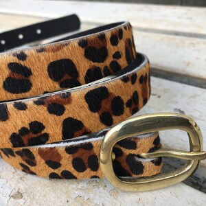 May include: A brown and black leopard print belt with a gold metal buckle. The belt is made of leather and has a smooth finish.