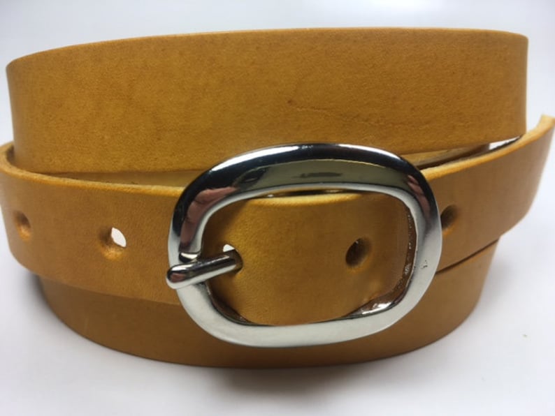 Puede incluir: Un cintur&oacute;n de cuero amarillo mostaza con una hebilla ovalada plateada.