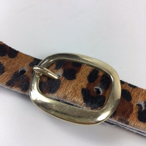 May include: A brown and black leopard print belt with a gold oval buckle.