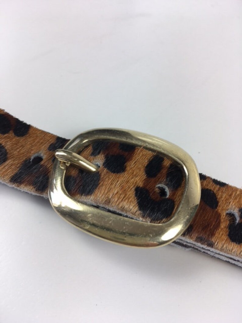 May include: A brown and black leopard print belt with a gold oval buckle.