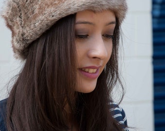 May include: A woman with long brown hair is wearing a brown faux fur headband. She is looking down and her expression is neutral.