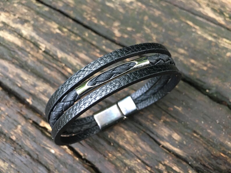 May include: Black leather bracelet with multiple strands, a braided center strand, and a silver-tone clasp. The bracelet has a textured appearance and a magnetic clasp. A stylish accessory.