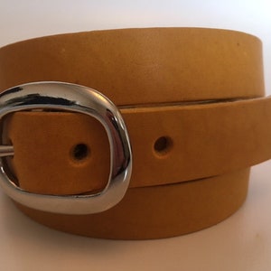 Puede incluir: Un cintur&oacute;n de cuero amarillo mostaza con una hebilla plateada. El cintur&oacute;n est&aacute; doblado por la mitad y la hebilla est&aacute; centrada en la imagen.